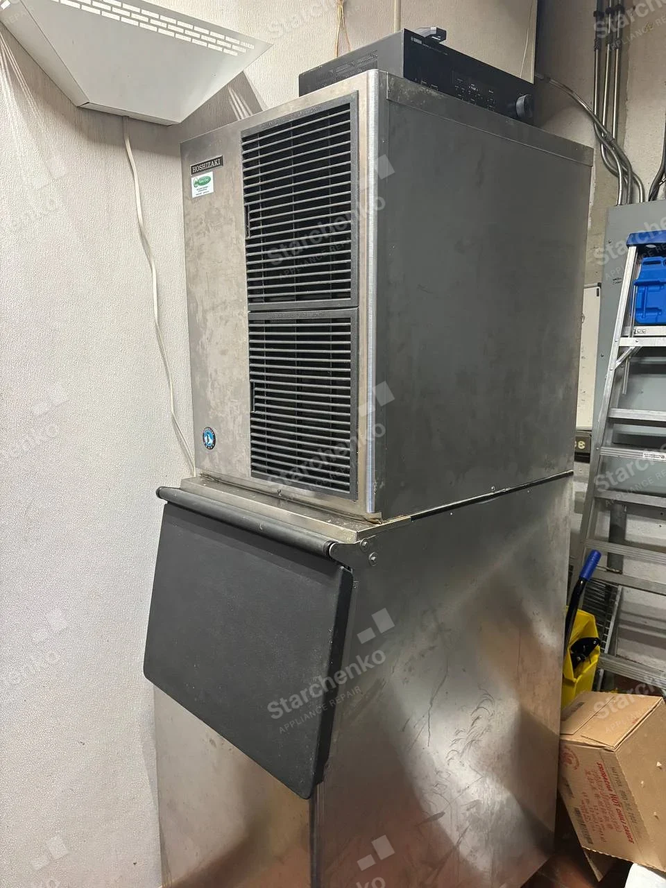 HOSHIZAKI badge on upper-left front of large commercial ice machine atop storage bin.