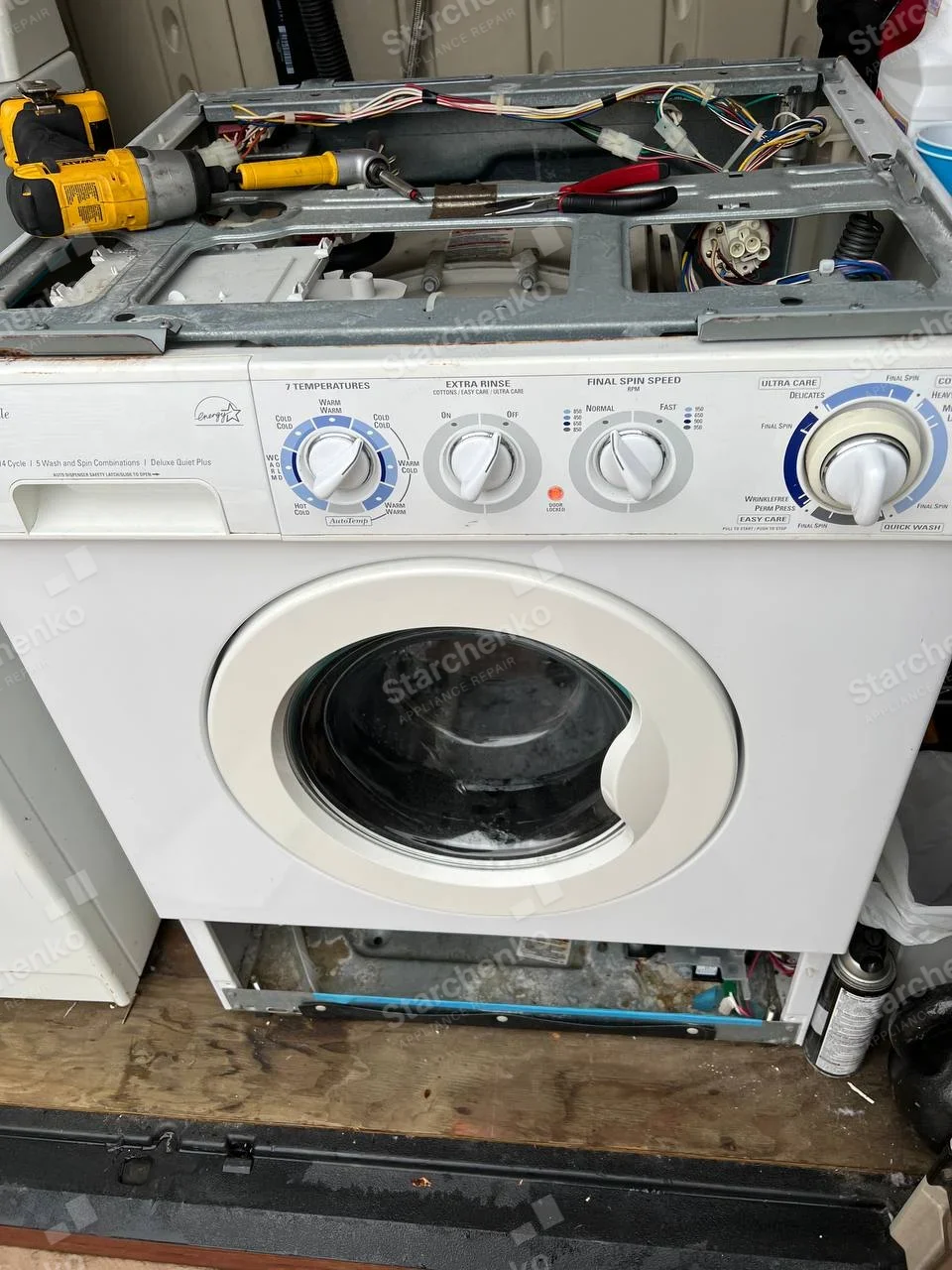 Kenmore repair: White front-load washer with top and lower panels removed, exposing wiring and components.