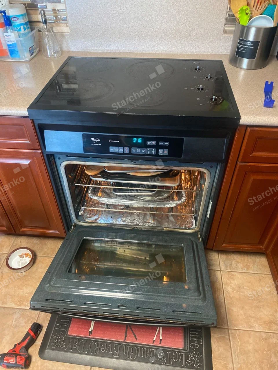 Black Whirlpool electric smooth-top range with oven door open and interior racks visible.