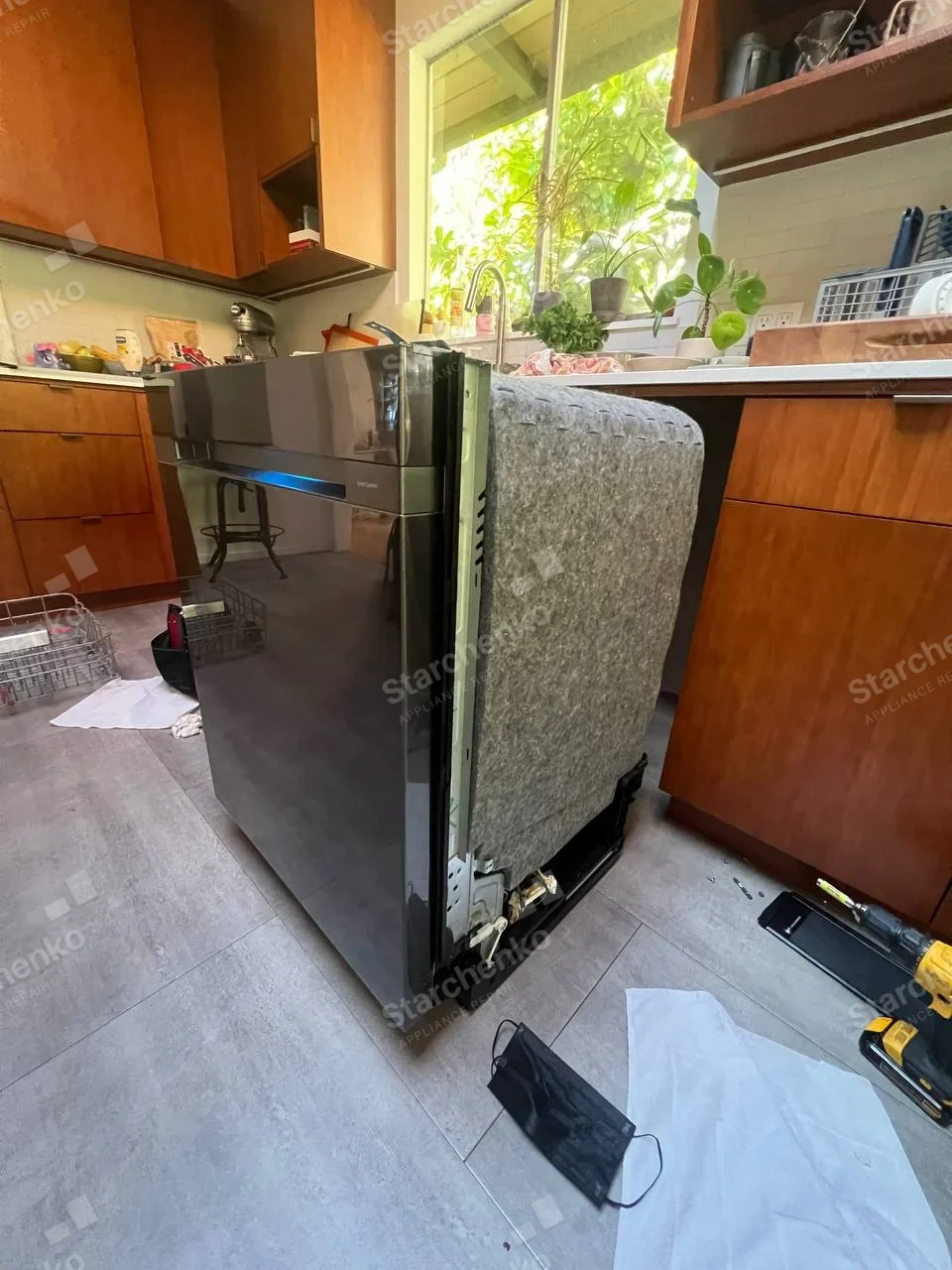 Samsung repair: Black-front built-in dishwasher pulled out from under the counter with side insulation exposed.