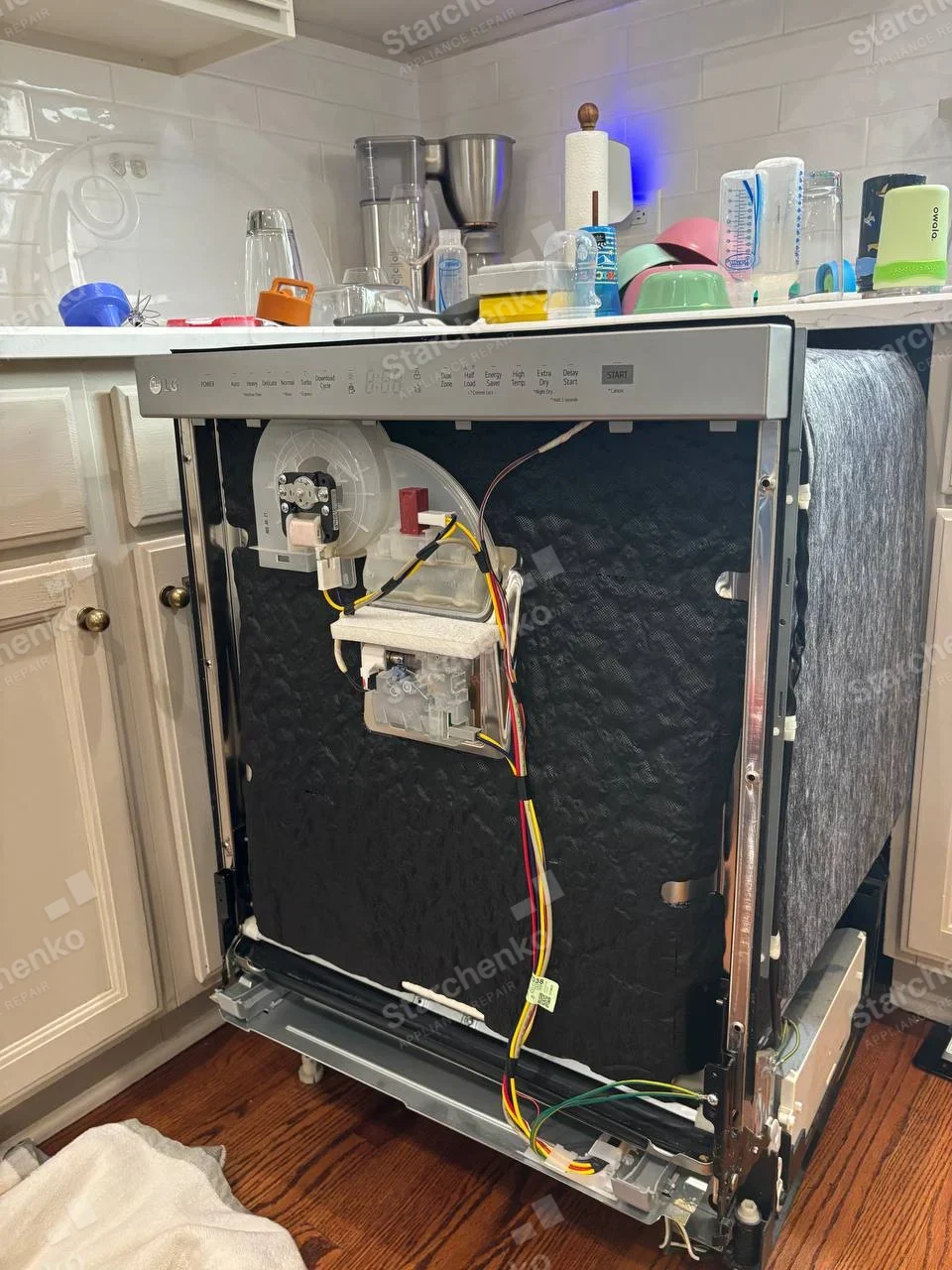 LG logo on upper-left front control strip of dishwasher pulled out of cabinet, side insulation and water assemblies exposed.