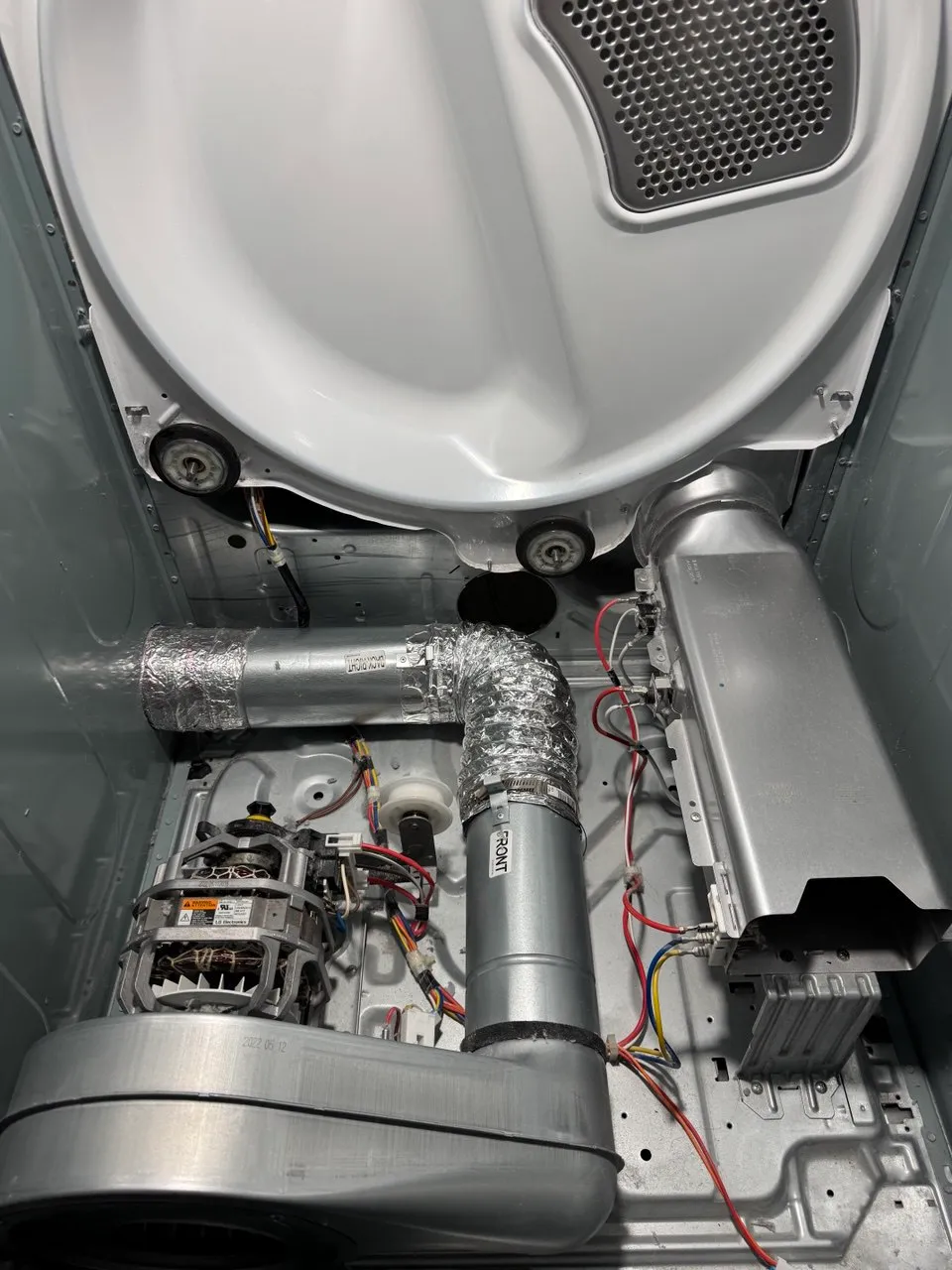 Dryer opened for repair with drum rollers, motor and blower visible