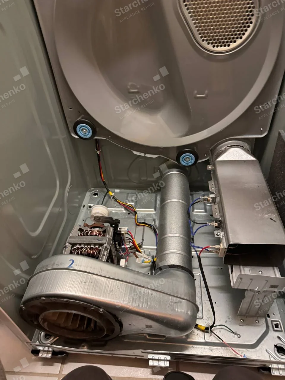 Maytag repair: Front-load dryer front opened, exposing drum support wheels, blower, motor, and heater duct.