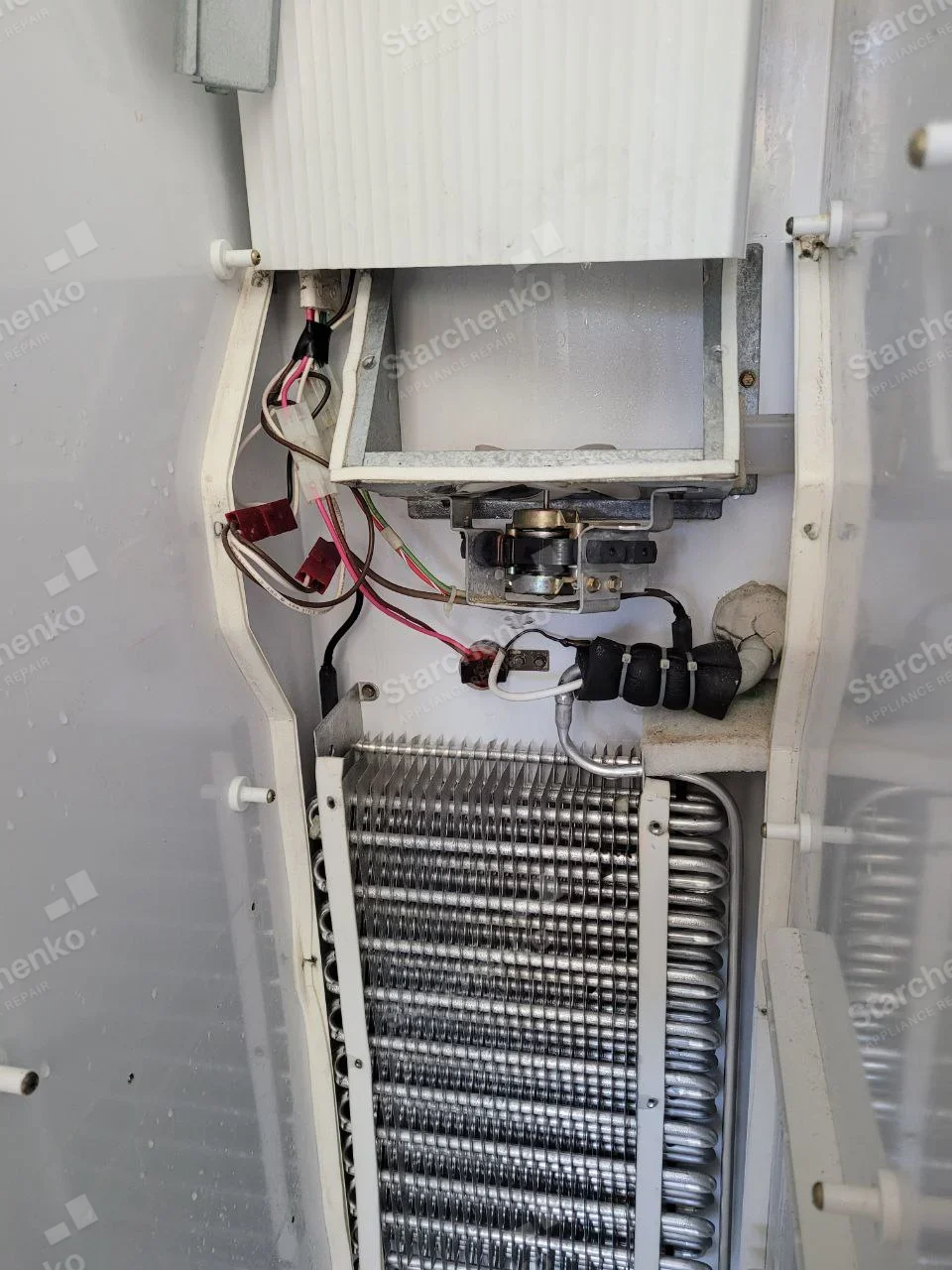 GE repair: Exposed refrigerator evaporator coil, fan mount and wiring inside an opened freezer compartment.