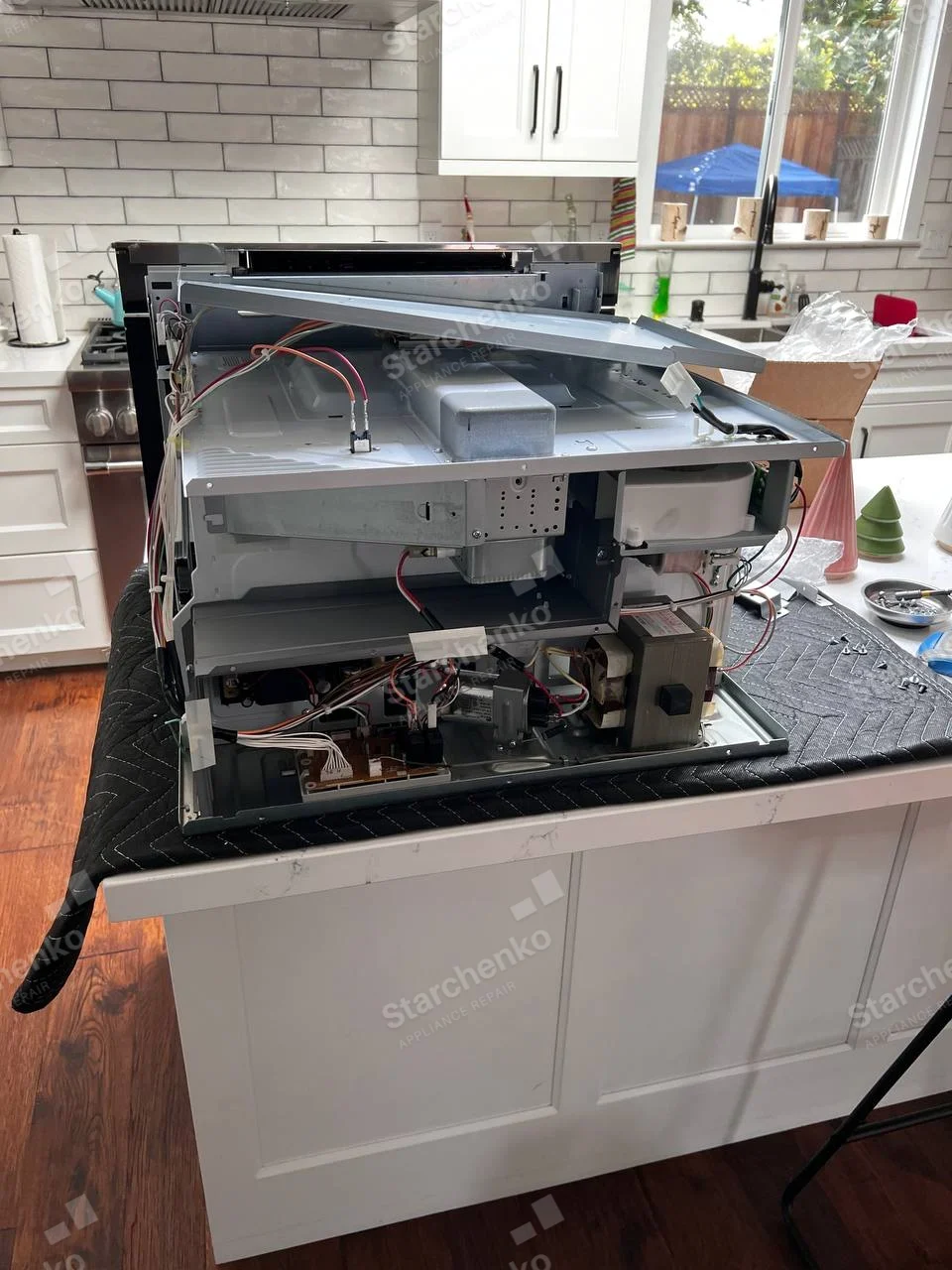 Samsung repair: Dismantled over-the-range microwave on kitchen island with transformer, wiring and circuit boards visible.