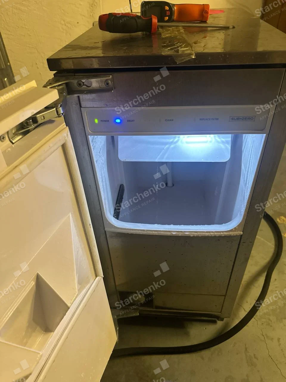 Sub-Zero repair: Undercounter standalone ice maker with open bin, illuminated control strip and no ice in bin.