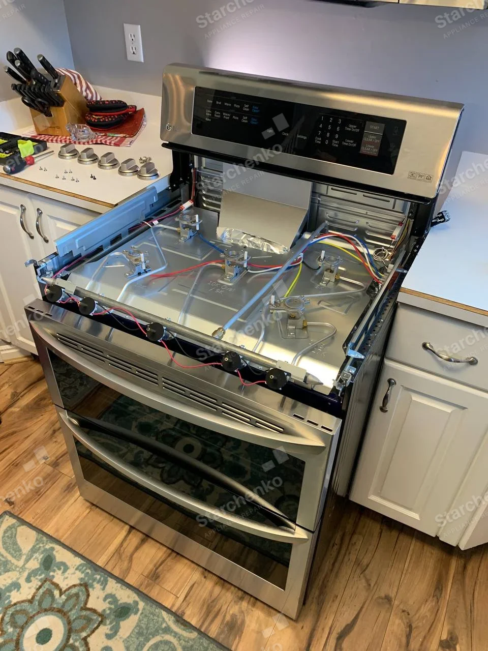 LG gas range with cooktop removed, showing gas valves and wires; knobs laid on countertop.