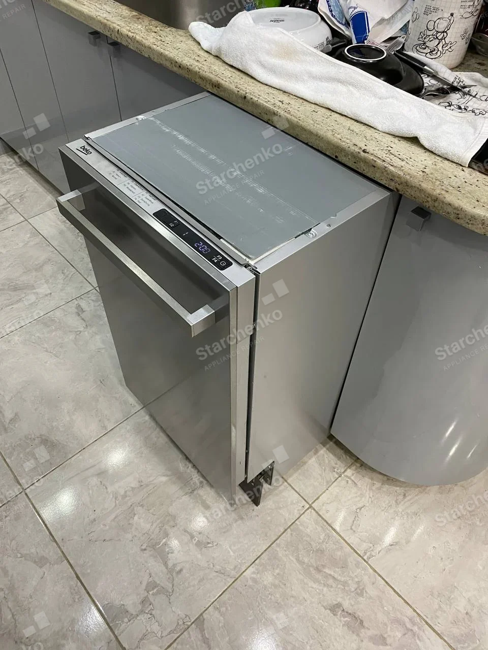 Beko stainless built-in dishwasher pulled partway from beneath countertop, top chassis visible.