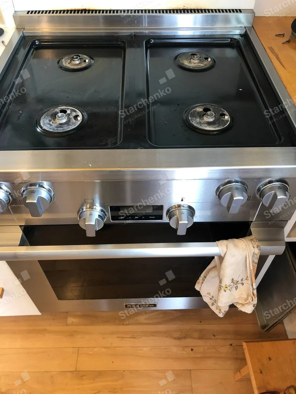 Miele gas range with four burner heads exposed and grates removed above oven.