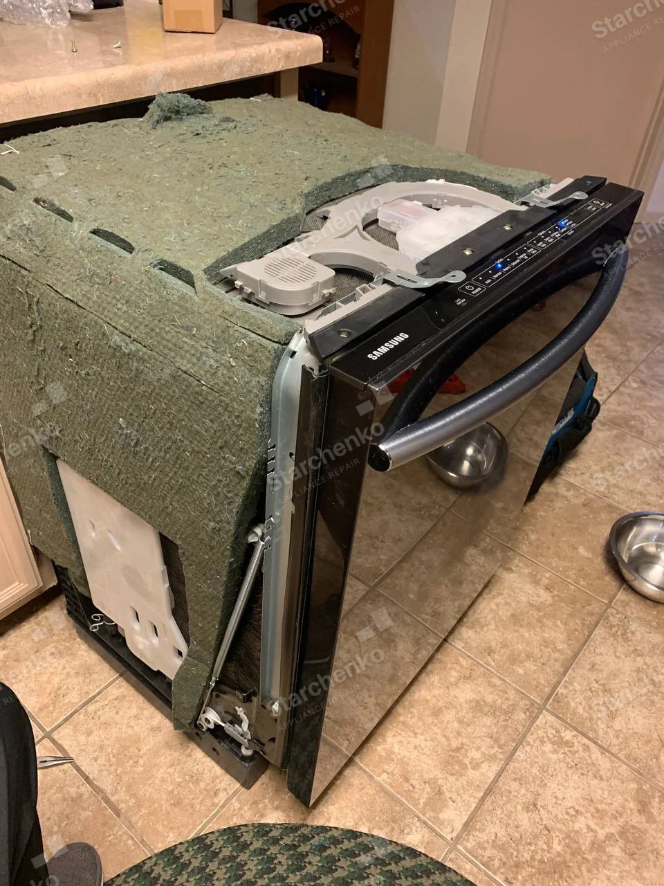 Black Samsung dishwasher removed from cabinetry with felt insulation visible around the housing.