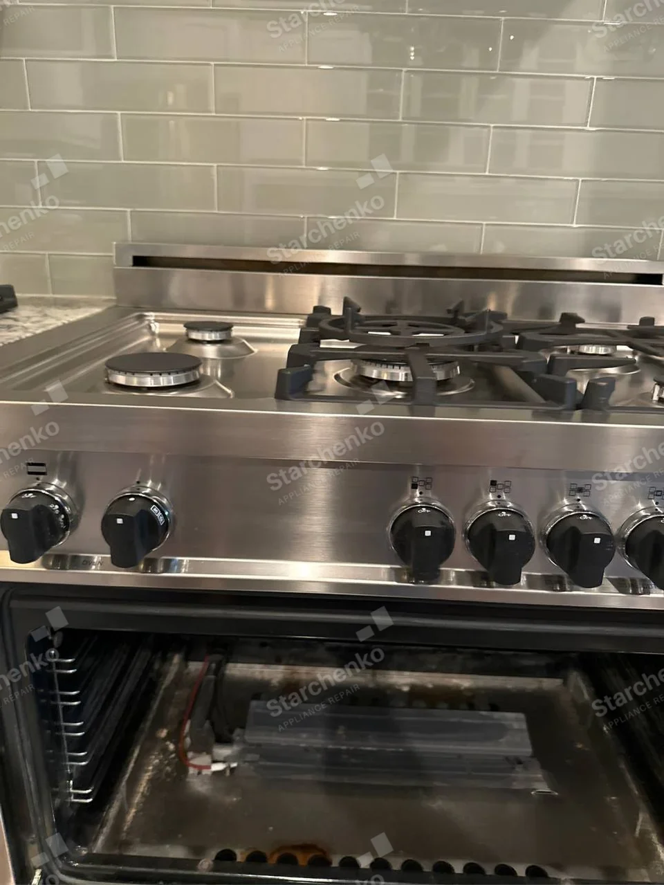 LG repair: Gas burners and front knobs above open oven cavity with a lower component removed.