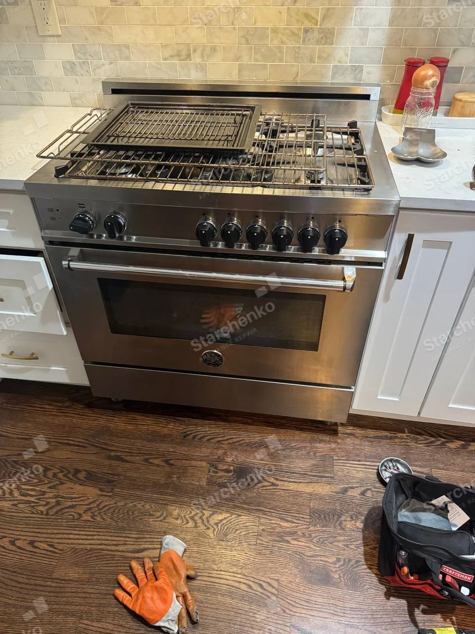 Round Bertazzoni badge on lower center oven door of gas range, burner grates lifted and caps removed.