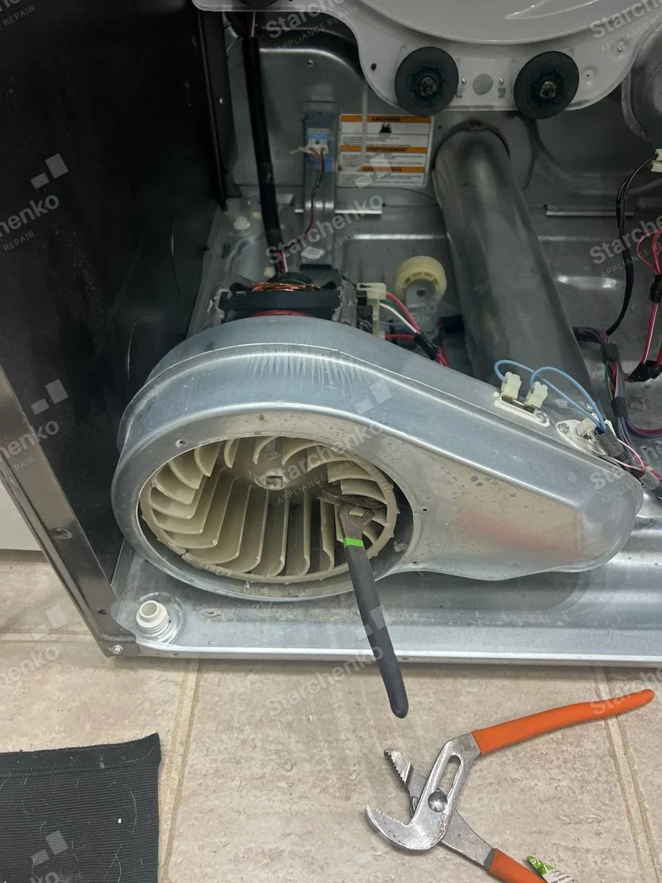 Maytag repair: Rear lower cabinet of a household dryer opened to expose blower wheel, motor and exhaust duct.