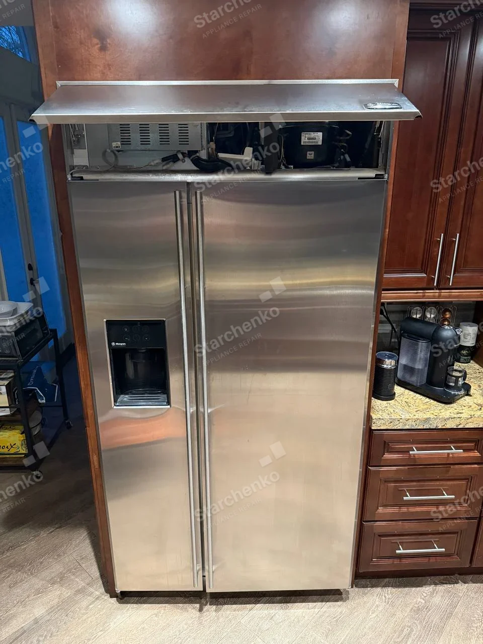 GE Monogram repair: Monogram mark on water dispenser of main side-by-side built-in refrigerator, upper compressor hatch open.