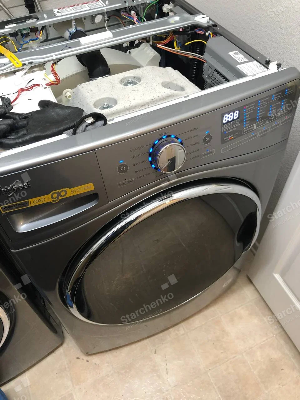 Whirlpool front-load washer with top panel removed, exposing tub and wiring.