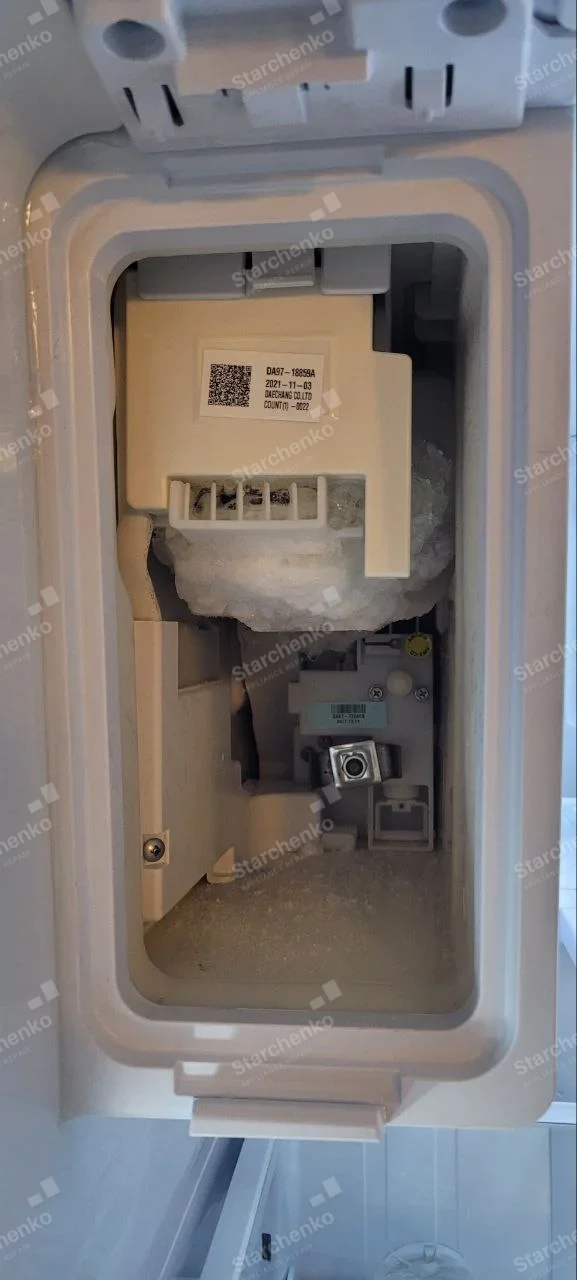 GE repair: Close-up of refrigerator ice-maker compartment with ice buildup around internal module.
