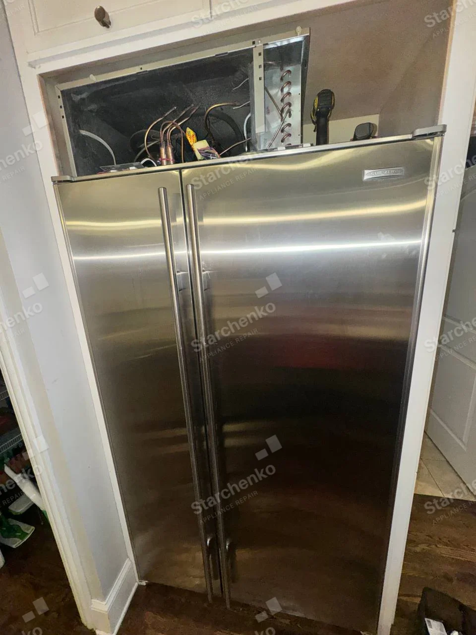Sub-Zero repair: Built-in side-by-side refrigerator with upper service panel removed, exposing refrigeration tubing and controls.