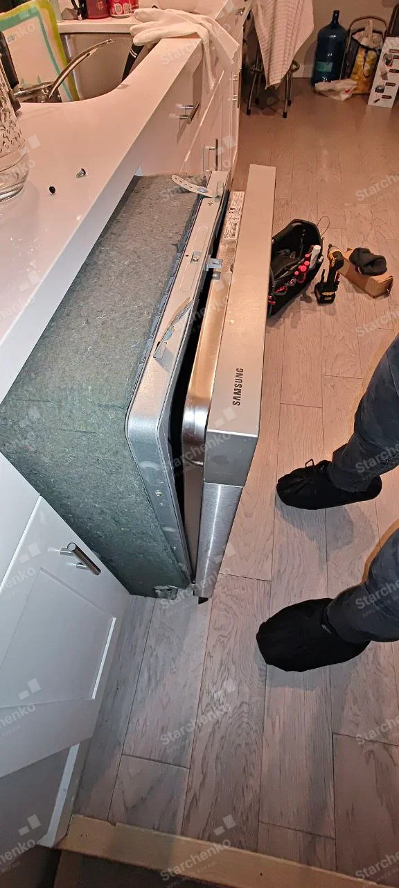 SAMSUNG name printed on door top edge of dishwasher pulled from cabinet, side insulation exposed.