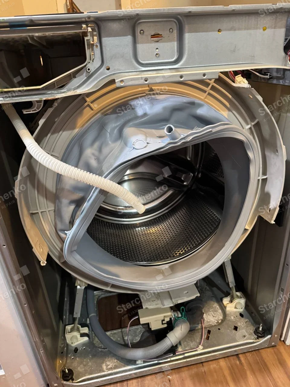 Electrolux repair: Front-load washer cabinet opened, with tub, door boot, and drain hose visible, no factory badge.