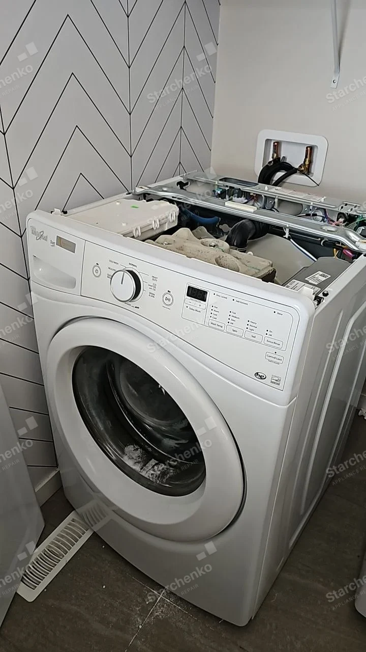 White Whirlpool front-load washer with top cover removed, exposing dispenser and hoses.