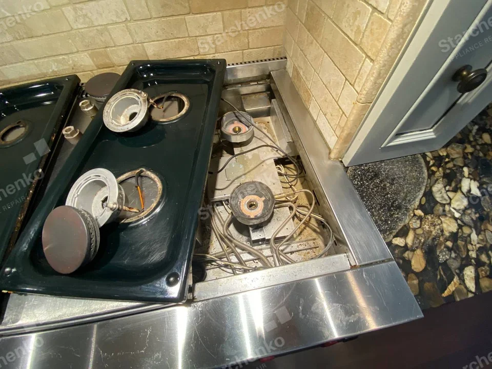 Kenmore repair: Gas range burner trays lifted from cooktop showing igniters and tubing, brand not visible.