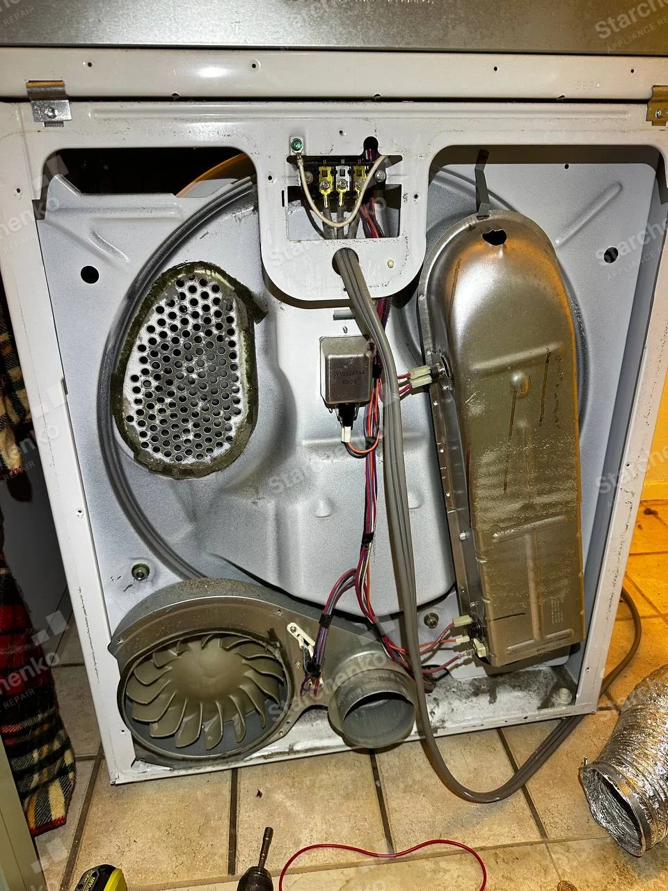 Electrolux repair: Rear cover removed from dryer, exposing heater housing, blower and exhaust outlet with flexible duct nearby.
