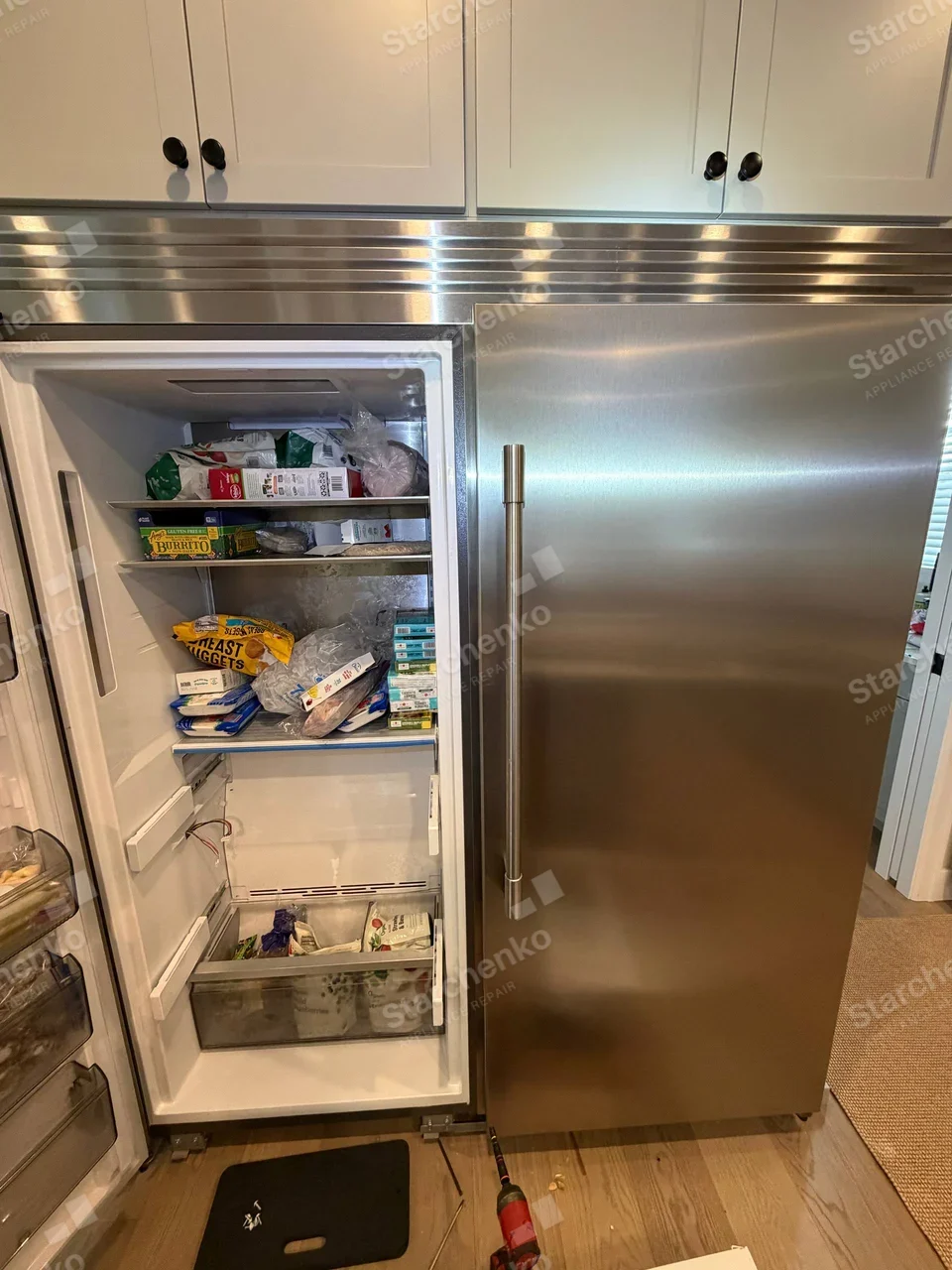 GE Monogram repair: Open freezer compartment of built-in side-by-side refrigerator, lower drawer removed and wiring visible, no maker mark.