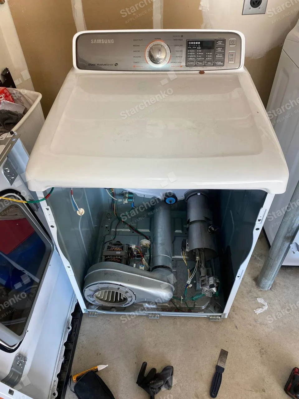 Samsung repair: Household front-load dryer with Steam MoistureSensor control panel, front panel removed exposing blower and motor.