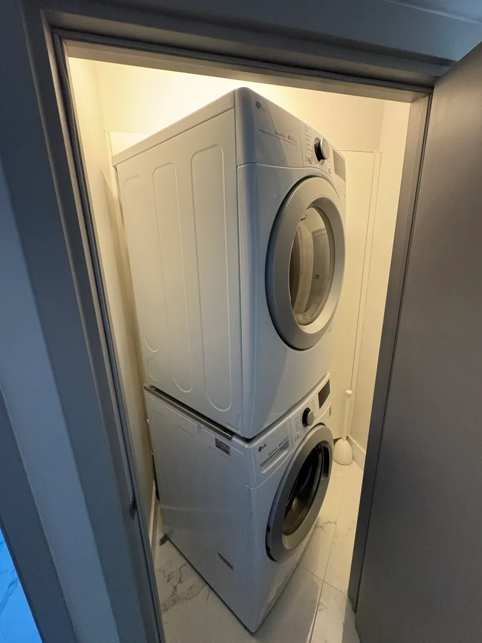 White LG dryer stacked above a washer in a narrow laundry closet