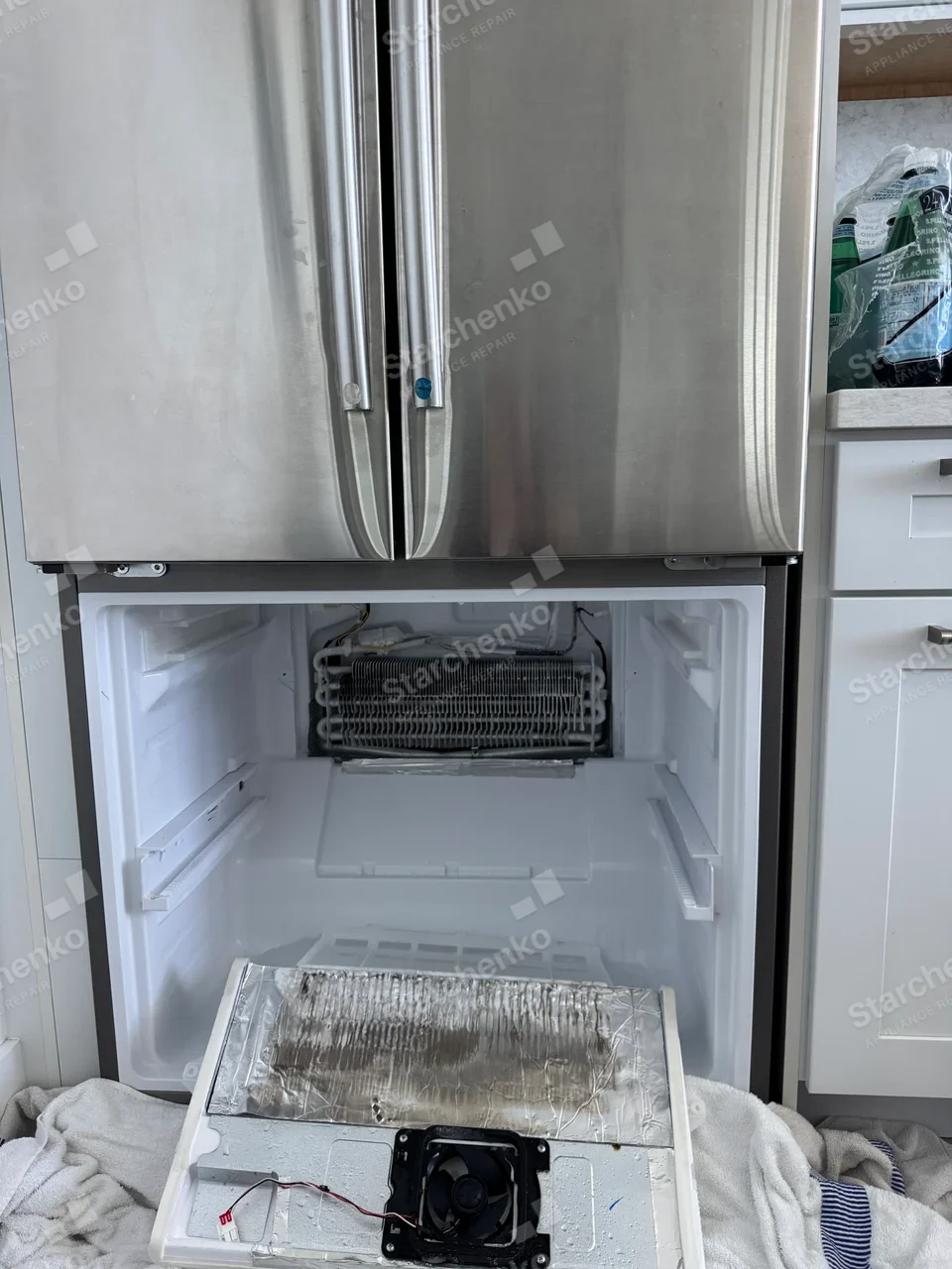 GE repair: French-door refrigerator with lower freezer liner open and evaporator exposed, small blue handle label not readable as factory brand.