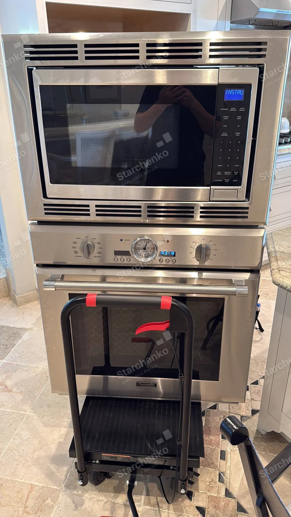 Thermador badge on lower built-in oven door, microwave mounted immediately above, service dolly in front.