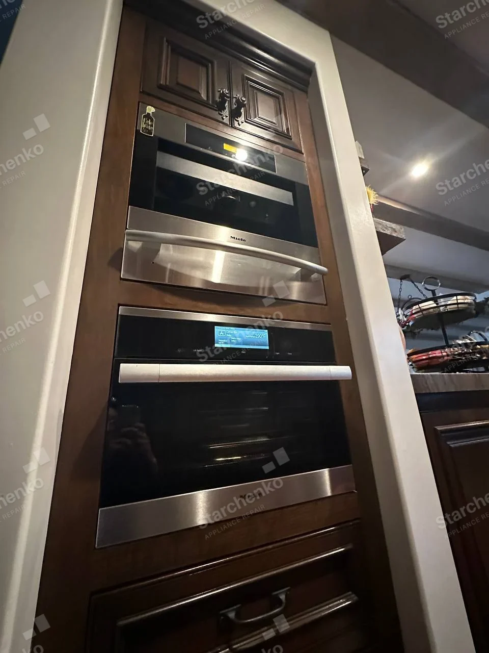 Miele built-in wall oven with lit display beneath a separate Miele microwave.