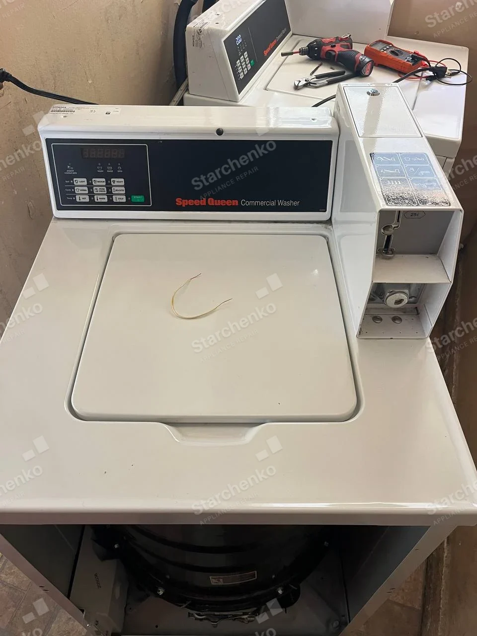 Coin-operated top-load commercial washer with front cabinet removed, another Speed Queen washer behind.