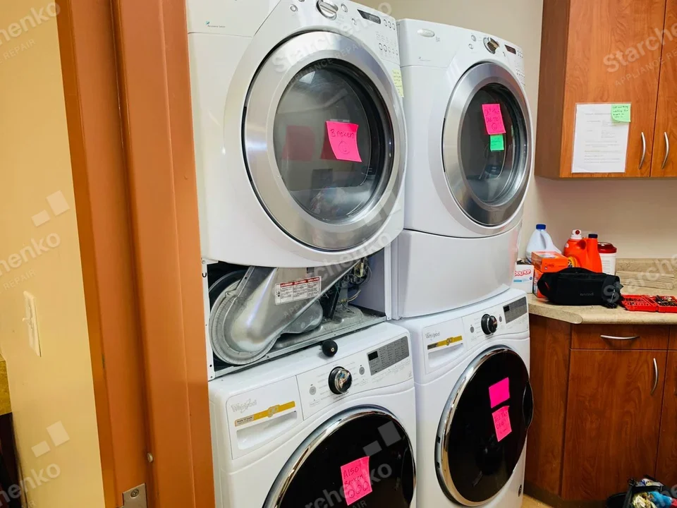 Electrolux repair: Left stacked dryer with lower front panel removed, exposing blower duct above washer.