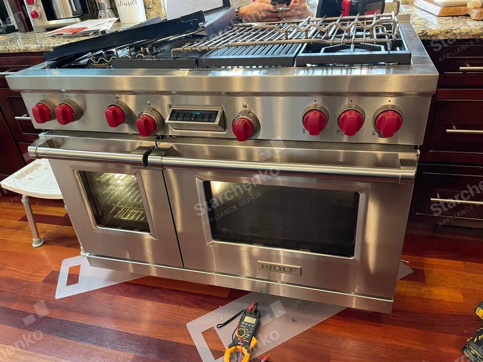 Wolf dual-oven gas range with red knobs, lifted grates and a test meter on the floor.