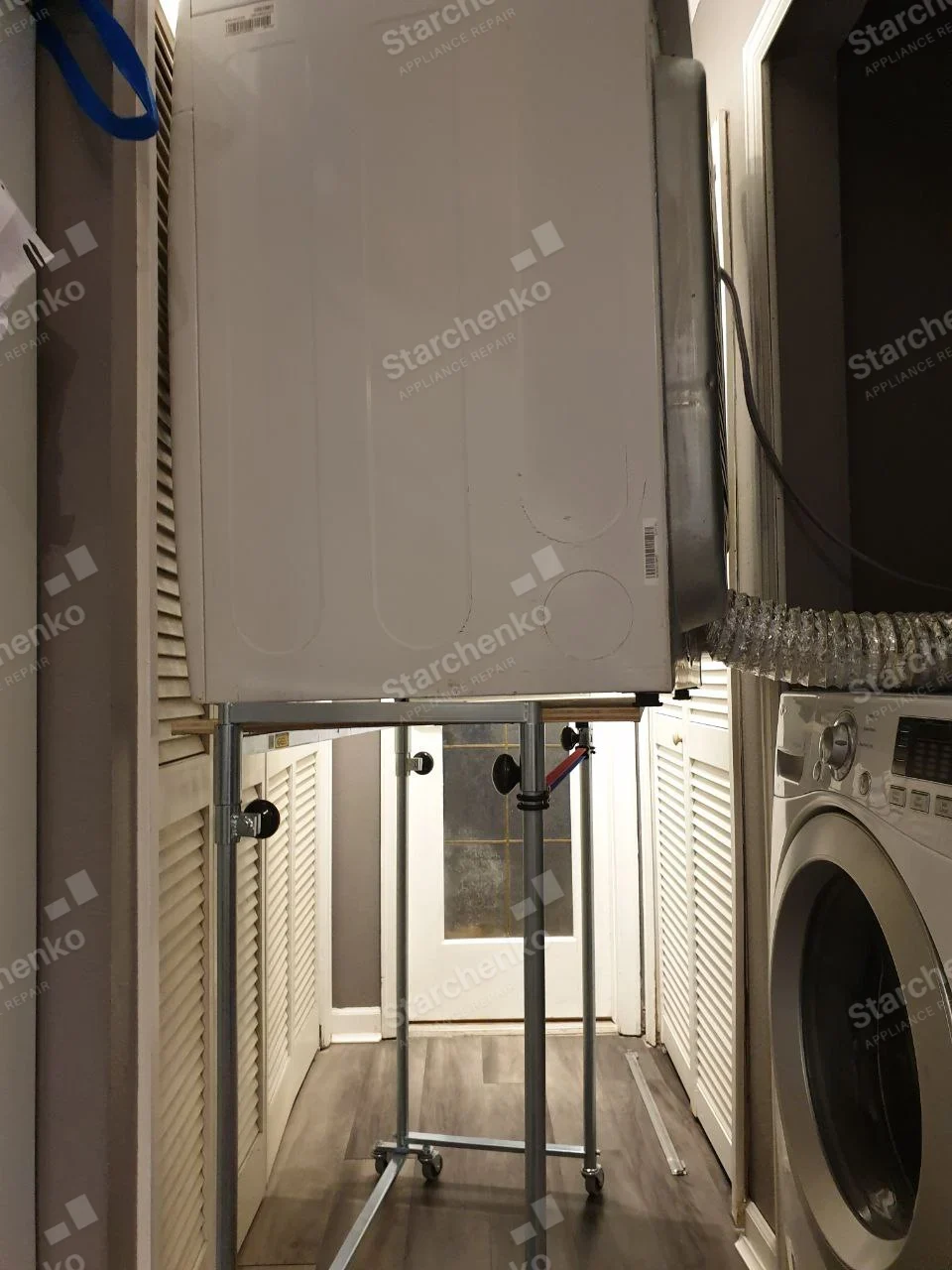 Kenmore dryer repair: Rear of front-load dryer removed from stacked position and elevated on wheeled stand, vent duct connected at side.