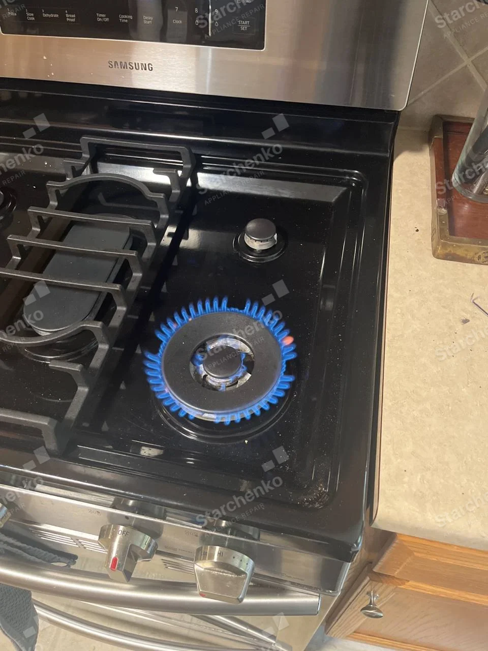 Samsung gas range with right front burner lit and blue flame visible.