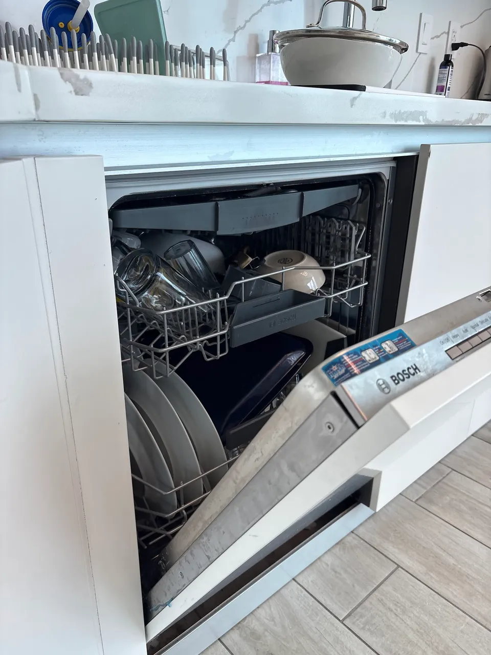 Bosch dishwasher open mid-repair with loaded racks in a white kitchen