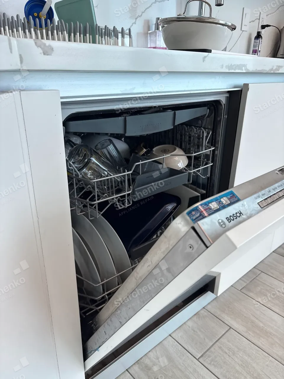 Bosch dishwasher open mid-repair with loaded racks in a white kitchen