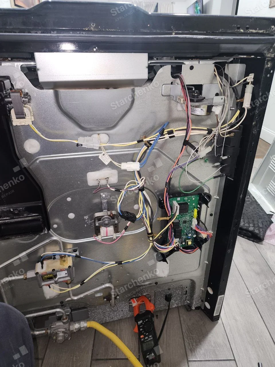 Kenmore repair: Rear of gas cooking appliance with burner gas supply, electrical controls, wiring and oven cavity behind panel.