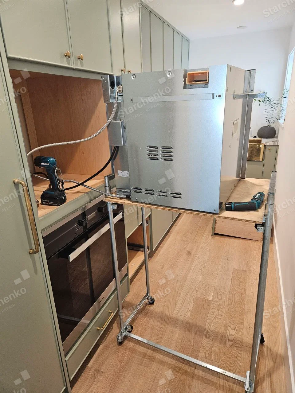 Frigidaire repair: Side of built-in wall oven pulled onto rolling service frame with vented metal housing visible.
