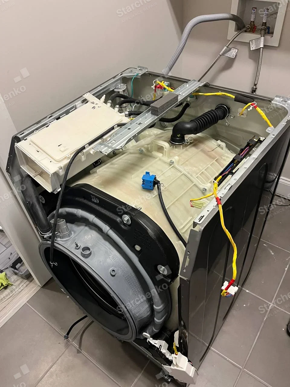 Electrolux repair: Dismantled front-load washer with tub, dispenser, hoses and wiring exposed.
