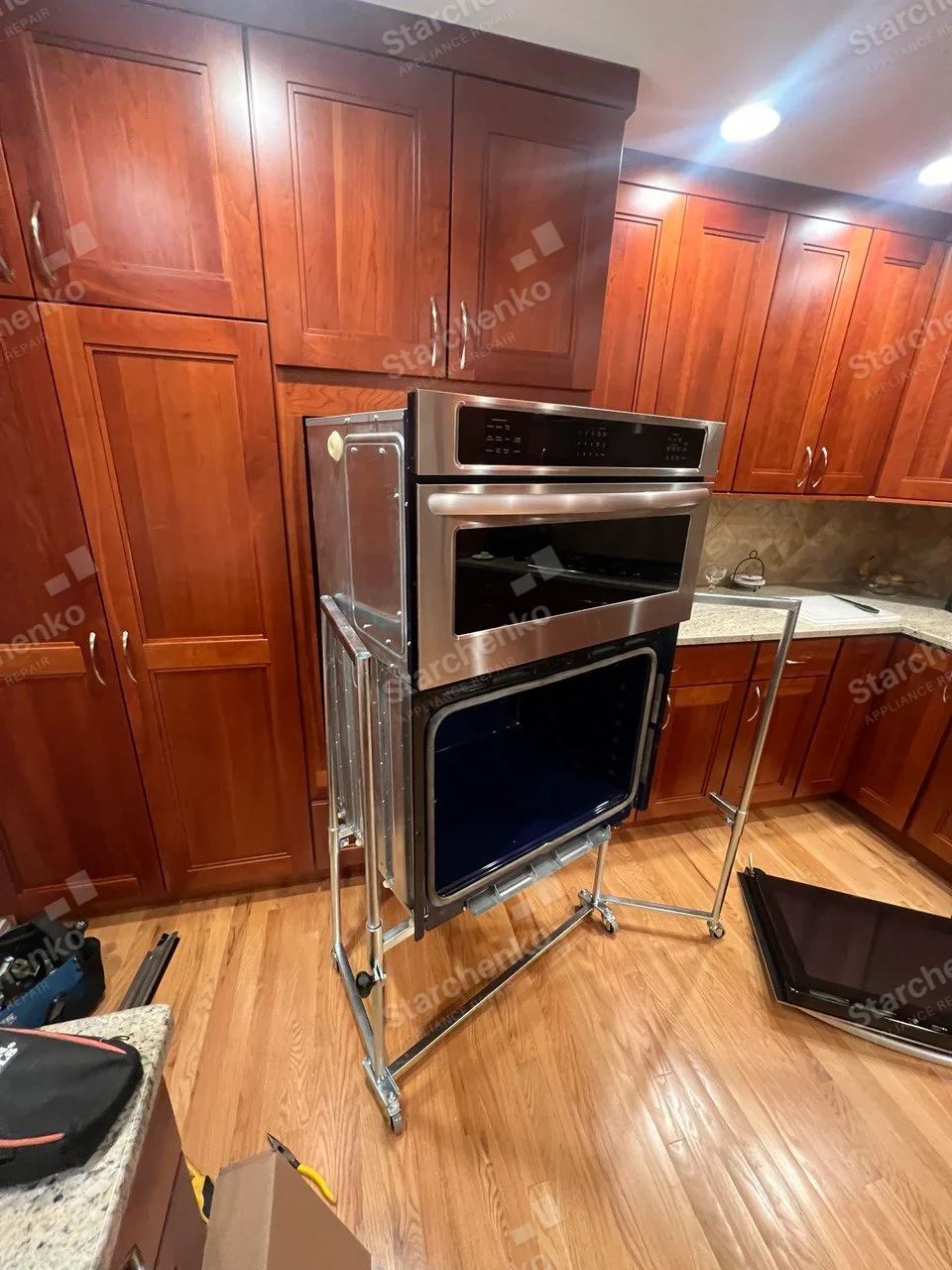 Frigidaire repair: Lower oven door removed from built-in stack on service cart, upper microwave/control unit separate within stack, no readable brand.