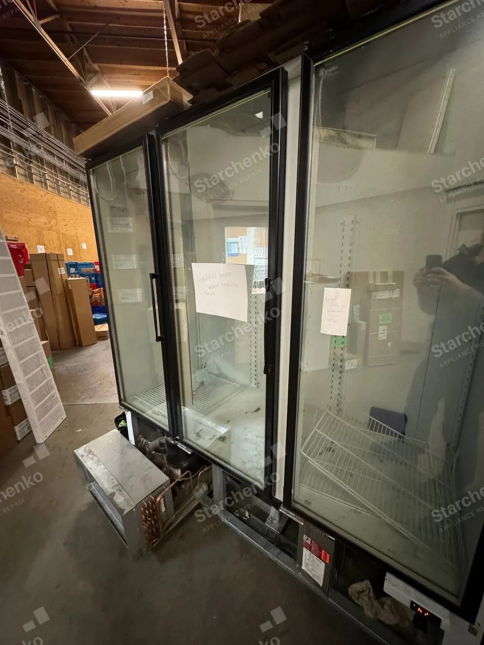 Beverage-Air repair: Tall glass-front three-door display refrigerator with lower compressor/condenser assembly removed on floor.