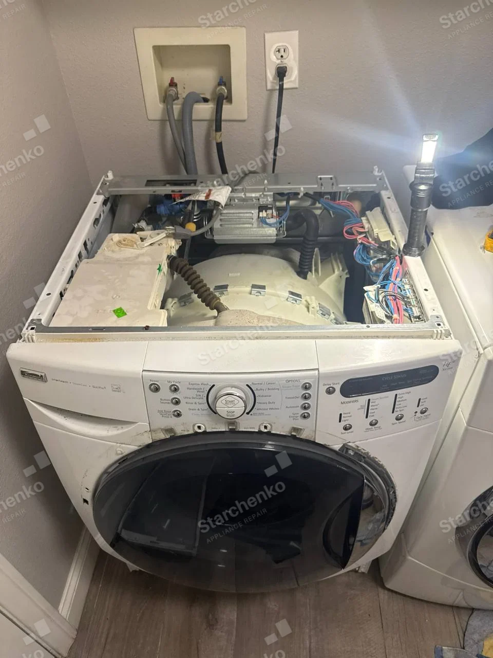 Kenmore badge on left of control fascia of front-load washer, top panel removed exposing tub and electronics.