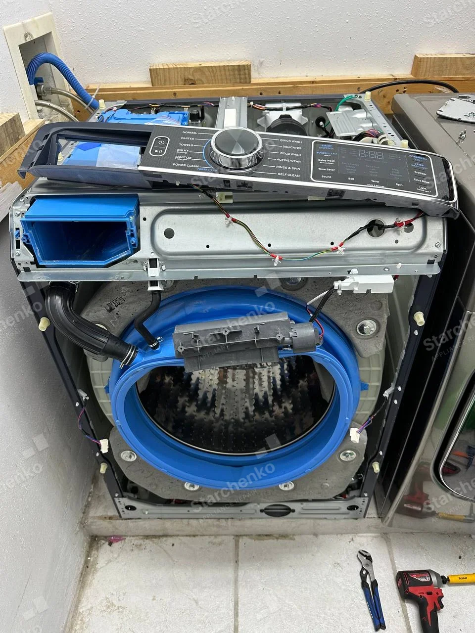 Front-load washer dismantled, blue door gasket, drum and detached control console showing Samsung lettering.