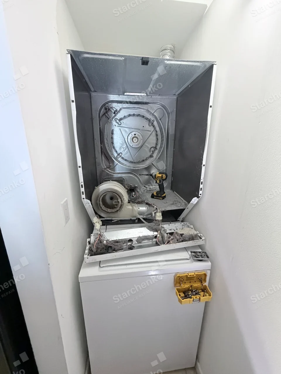 Kenmore dryer repair: Rear panel removed from upper dryer of laundry stack, exposing heater and blower, lower washer is not the repair target.