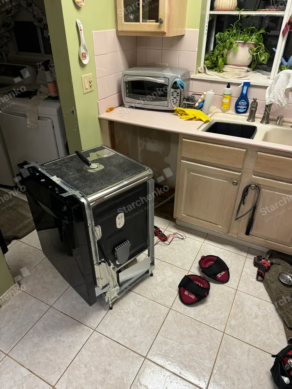 Black GE dishwasher rolled out to the middle of the kitchen for repair