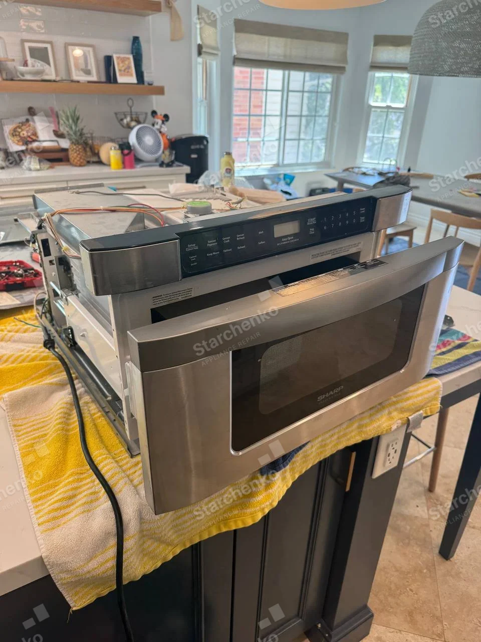 Sharp repair: Microwave oven removed from mounting, with its top cover off and control wiring exposed.