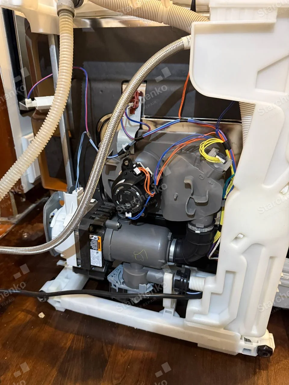 Samsung repair: Dishwasher underside opened with drain pump, circulation motor and hoses visible, no main-appliance brand.